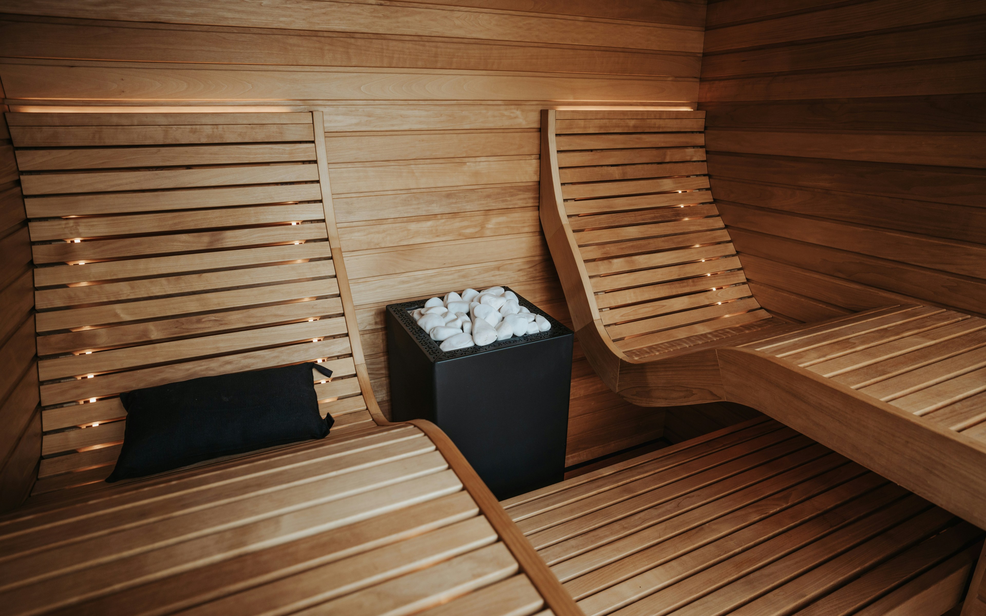 Moderne Sauna aus Holz mit Bänken und Ofen, konzipiert für Entspannung und Hautregeneration