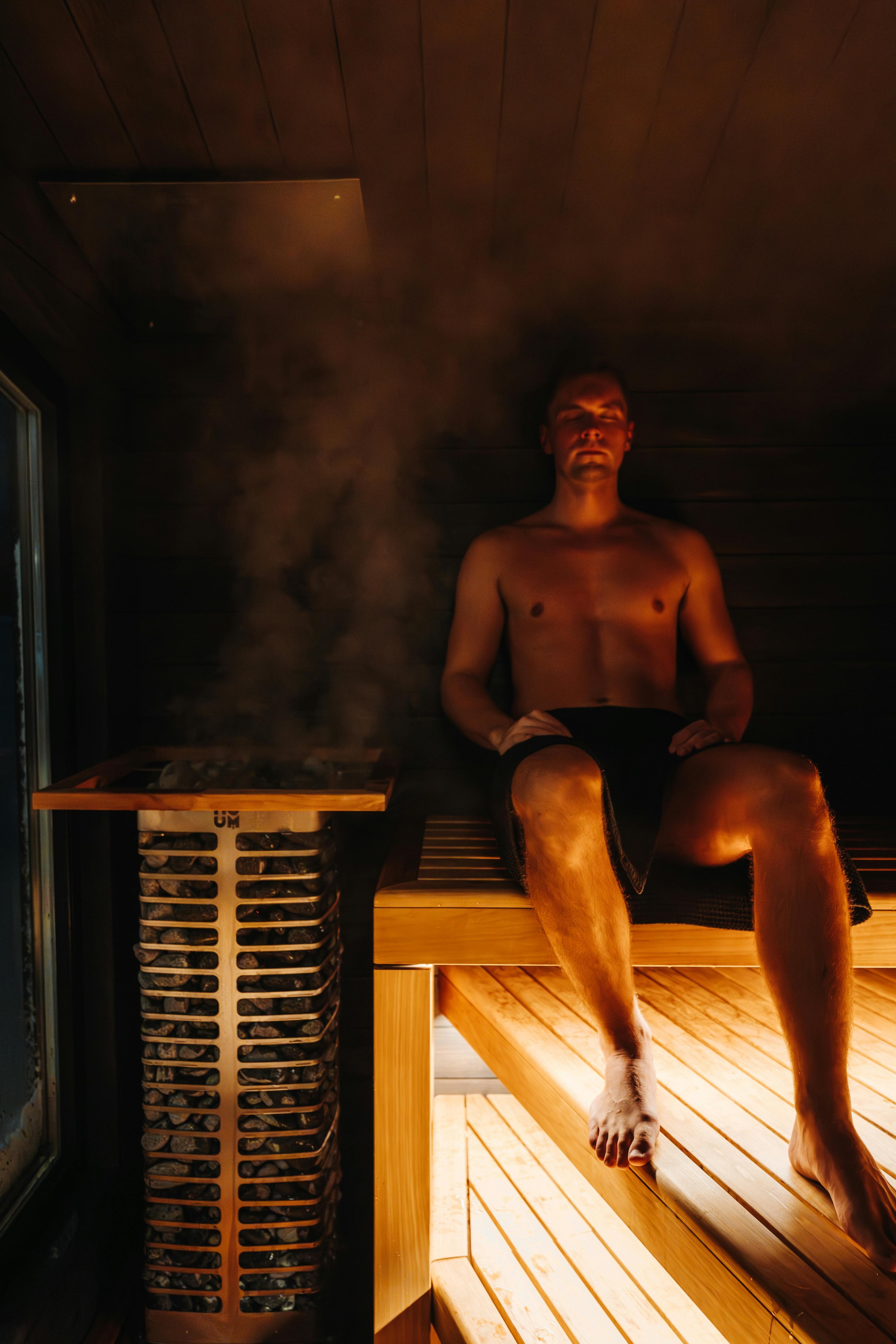 Ein Mann sitzt in einer Sauna neben einem dampfenden Saunaofen.