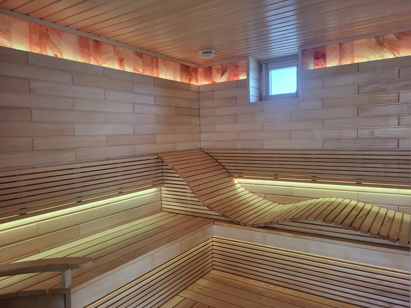 Helle Holzsauna mit gewellter Sitzbank und LED-Beleuchtung.