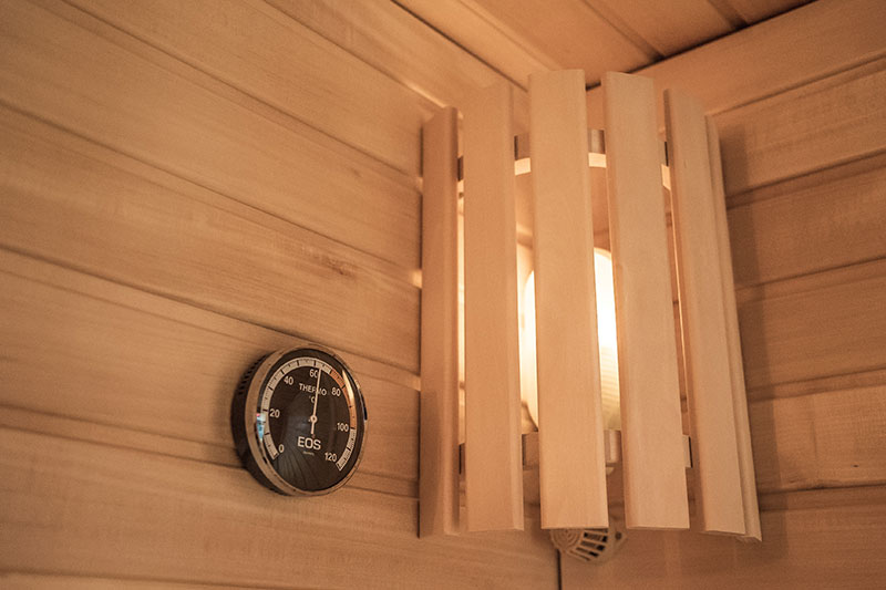 EOS-Saunathermometer und Holzlampenschirm in der Ecke.