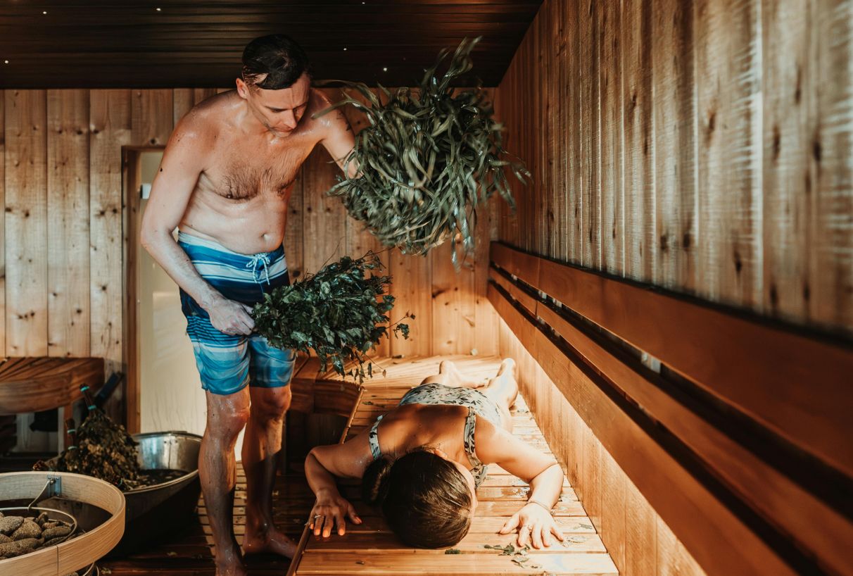 Ein Mann schlägt eine Frau in der Sauna mit einem Birkenzweig – ein traditionelles Saunaritual zur Entspannung